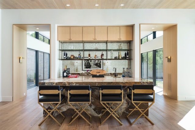 bar featuring light hardwood / wood-style floors, wood ceiling, backsplash, and light brown cabinetry