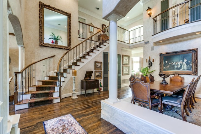 dining space featuring a high ceiling, dark hardwood / wood-style flooring, crown molding, and ornate columns