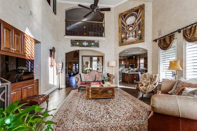 living room featuring ceiling fan, dark wood-type flooring, a towering ceiling, and crown molding