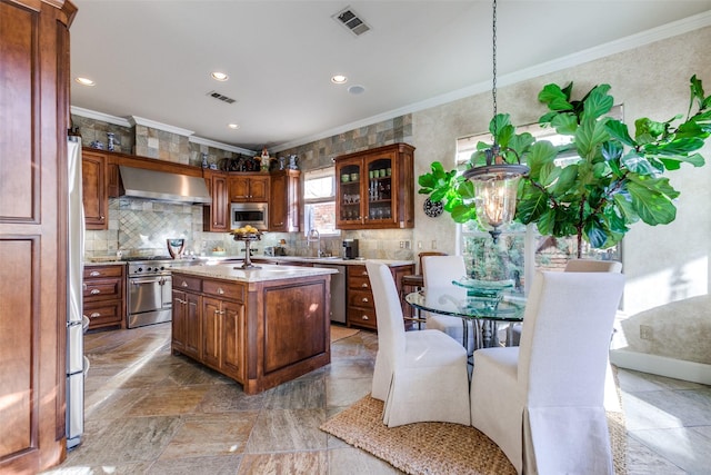 kitchen with a kitchen island, appliances with stainless steel finishes, wall chimney range hood, and crown molding