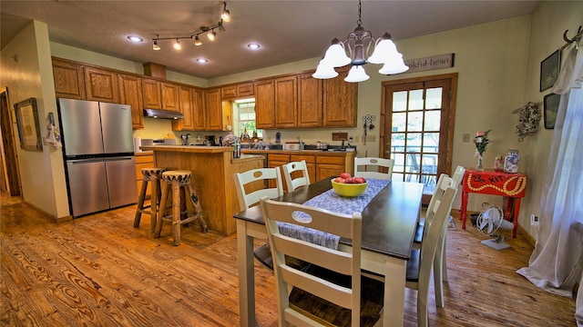 kitchen featuring stainless steel refrigerator, a center island, an inviting chandelier, decorative light fixtures, and light wood-type flooring