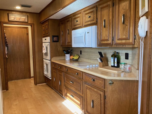 kitchen with a textured ceiling, tasteful backsplash, light hardwood / wood-style floors, and white appliances