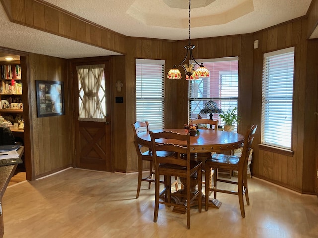 dining area featuring a textured ceiling, an inviting chandelier, a raised ceiling, and wooden walls