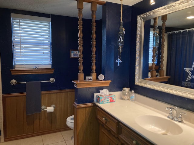 bathroom with tile patterned floors, vanity, a textured ceiling, toilet, and wood walls