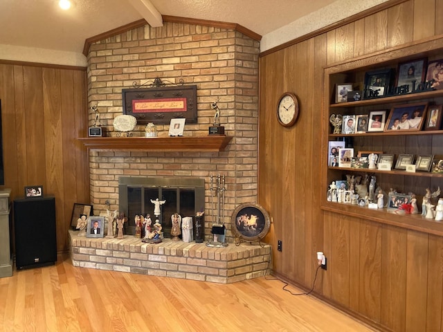 living room with wooden walls, a brick fireplace, vaulted ceiling with beams, light wood-type flooring, and a textured ceiling