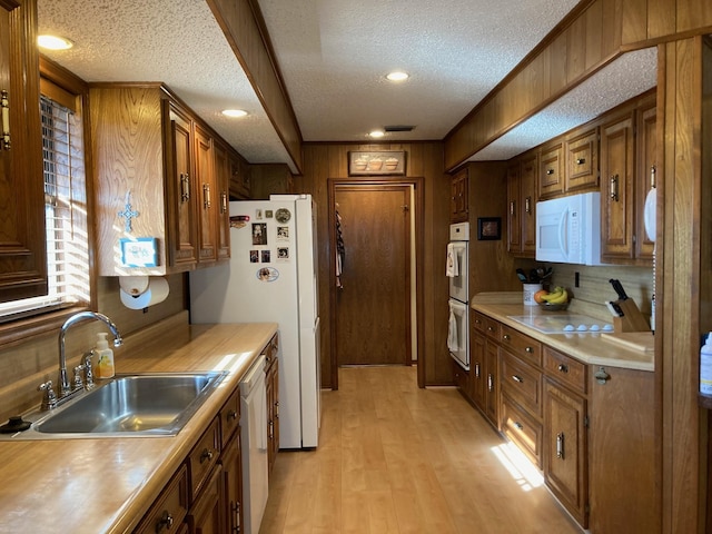 kitchen featuring wood walls, white appliances, sink, a textured ceiling, and light hardwood / wood-style floors