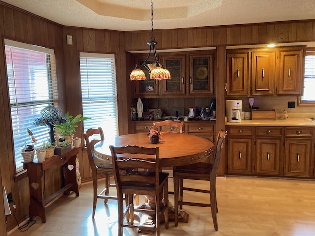 dining room with wood walls, a textured ceiling, a wealth of natural light, and light hardwood / wood-style flooring