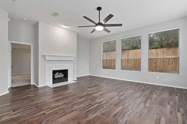 unfurnished living room featuring a high end fireplace, dark hardwood / wood-style flooring, and ceiling fan