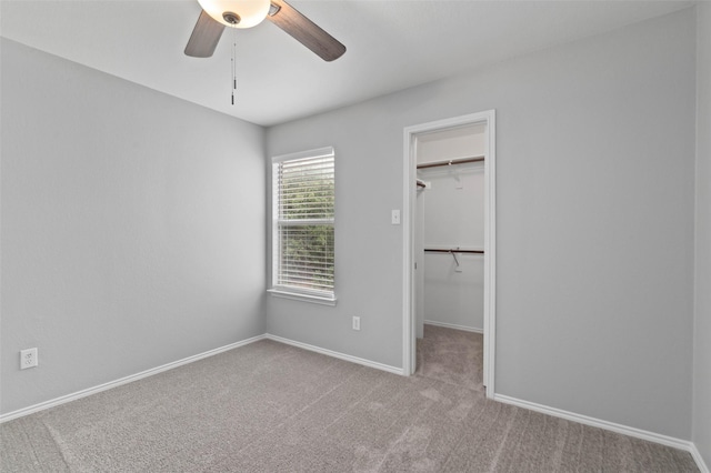 unfurnished bedroom with a walk in closet, ceiling fan, a closet, and light carpet