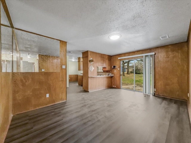 unfurnished living room featuring dark hardwood / wood-style floors, a textured ceiling, and wooden walls