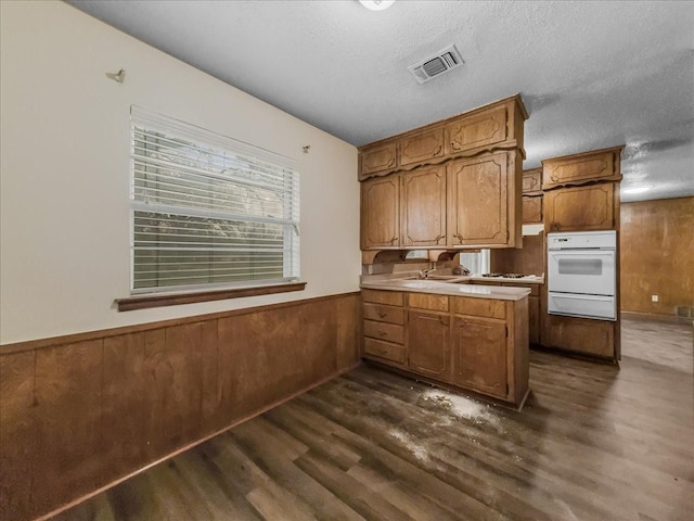 kitchen featuring a textured ceiling, dark hardwood / wood-style flooring, wooden walls, kitchen peninsula, and white oven