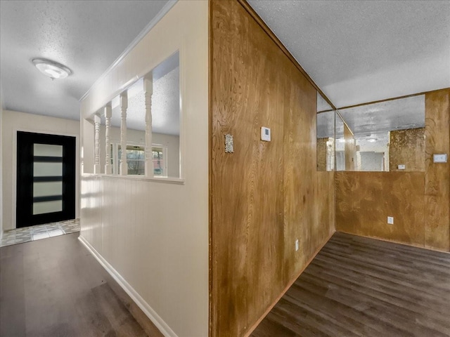 corridor featuring ornamental molding, dark wood-type flooring, a textured ceiling, and wood walls