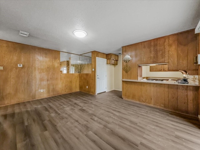 kitchen featuring wooden walls, kitchen peninsula, a textured ceiling, and light wood-type flooring