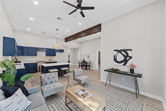 living room featuring beam ceiling, light hardwood / wood-style flooring, ceiling fan, and sink