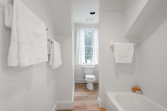 bathroom with toilet, wood-type flooring, and a tub to relax in