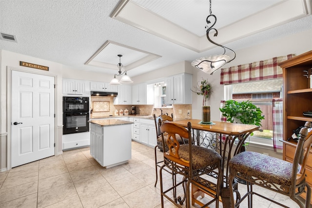 kitchen featuring light tile patterned floors, a kitchen island, pendant lighting, black double oven, and white cabinets