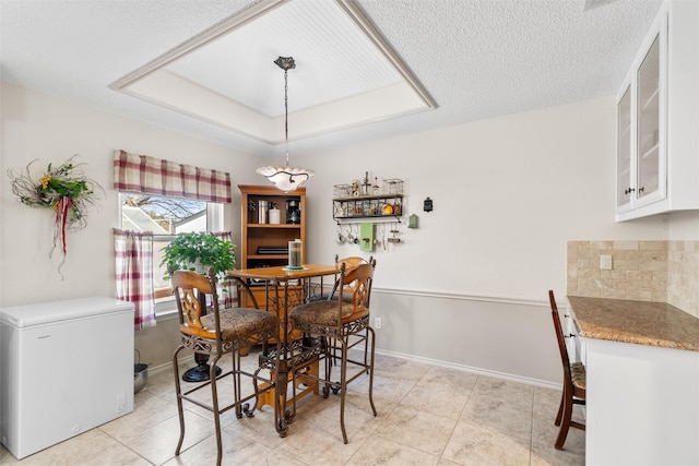 dining area with a raised ceiling, a textured ceiling, and light tile patterned flooring