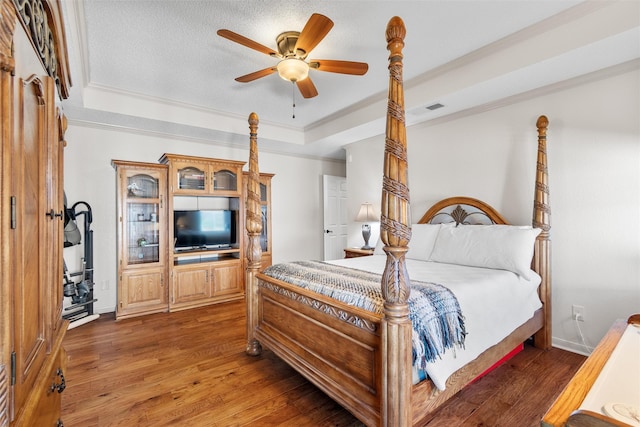 bedroom featuring crown molding, a tray ceiling, dark hardwood / wood-style floors, and ceiling fan