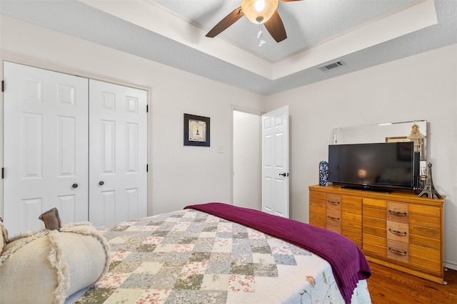 bedroom with hardwood / wood-style flooring, ceiling fan, a textured ceiling, a raised ceiling, and a closet