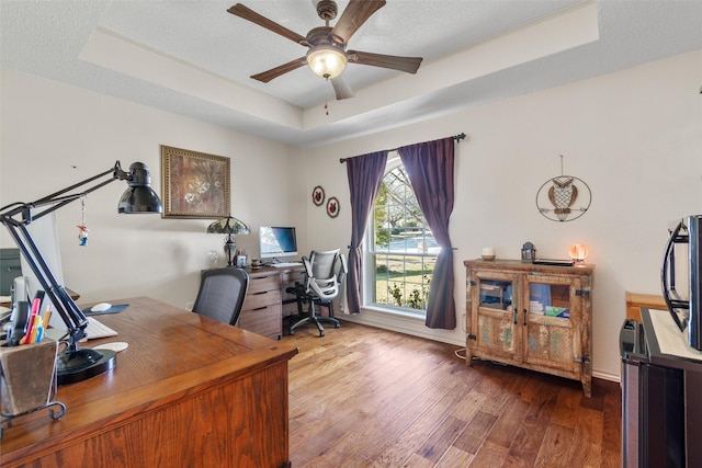 office area with hardwood / wood-style floors, a tray ceiling, a textured ceiling, and ceiling fan