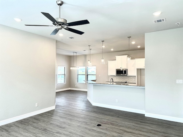 kitchen with light stone counters, dark wood-type flooring, tasteful backsplash, white cabinets, and ceiling fan