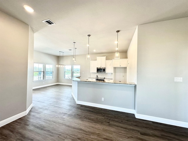 kitchen featuring appliances with stainless steel finishes, hanging light fixtures, light stone countertops, dark wood-type flooring, and white cabinets