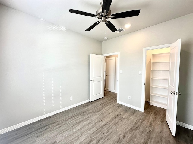 unfurnished bedroom featuring ceiling fan, a spacious closet, a closet, and hardwood / wood-style flooring