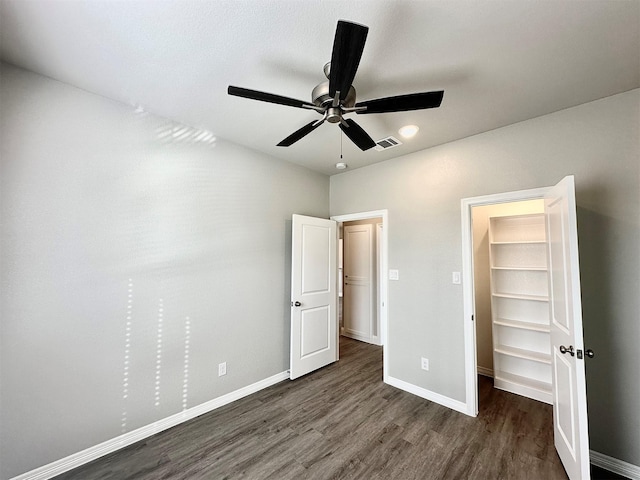 unfurnished bedroom featuring dark wood-type flooring, a closet, ceiling fan, and a spacious closet