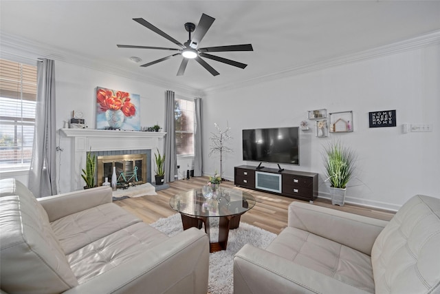 living room featuring ceiling fan, wood-type flooring, a fireplace, and ornamental molding