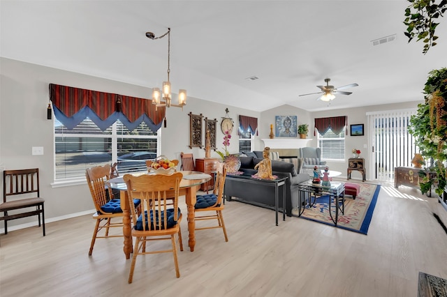 dining room with ceiling fan with notable chandelier, light wood-type flooring, and vaulted ceiling