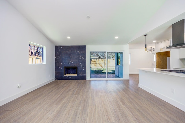 unfurnished living room featuring a high end fireplace, light wood-type flooring, and vaulted ceiling