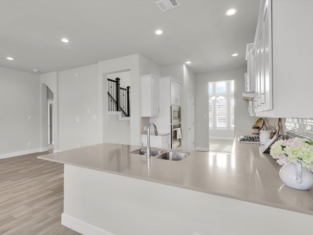 kitchen with kitchen peninsula, stainless steel appliances, light wood-type flooring, white cabinets, and sink