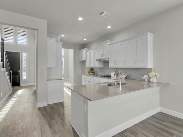 kitchen featuring light hardwood / wood-style floors, kitchen peninsula, stainless steel gas stovetop, sink, and white cabinetry