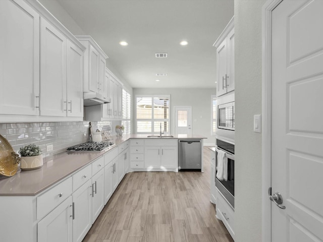 kitchen featuring light hardwood / wood-style floors, stainless steel appliances, sink, white cabinetry, and tasteful backsplash