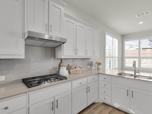 kitchen featuring light wood-type flooring, stainless steel gas cooktop, backsplash, white cabinetry, and sink