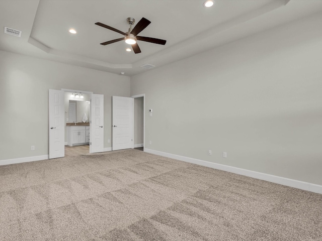 unfurnished bedroom with ceiling fan, light carpet, ensuite bath, and a tray ceiling