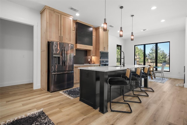 kitchen with appliances with stainless steel finishes, tasteful backsplash, a kitchen island with sink, pendant lighting, and light hardwood / wood-style floors