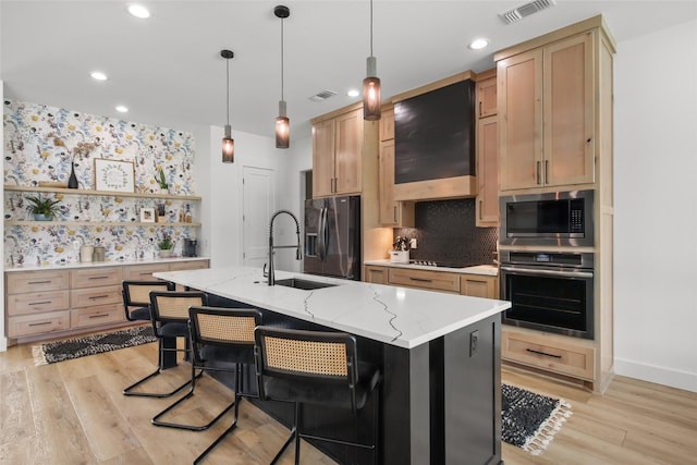 kitchen featuring appliances with stainless steel finishes, light stone counters, custom exhaust hood, sink, and a center island with sink