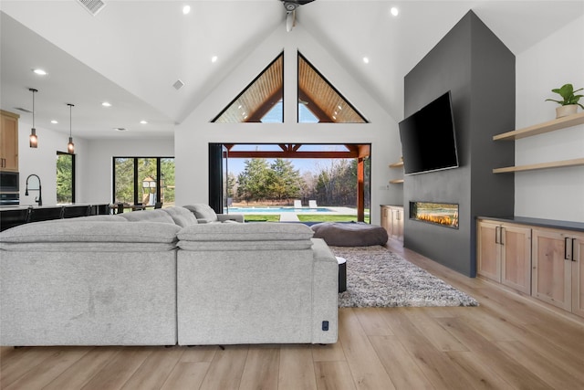 living room featuring ceiling fan, light wood-type flooring, sink, and high vaulted ceiling