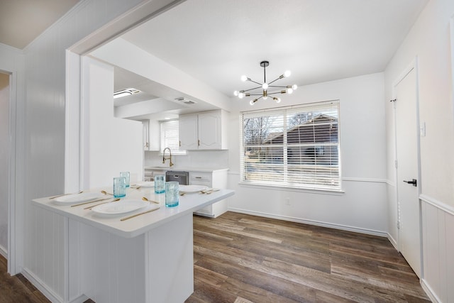 kitchen featuring kitchen peninsula, stainless steel dishwasher, sink, white cabinets, and a chandelier