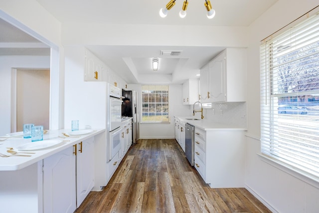 kitchen featuring backsplash, white cabinets, sink, stainless steel dishwasher, and dark hardwood / wood-style flooring