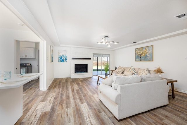 living room with a brick fireplace, washer and clothes dryer, crown molding, light hardwood / wood-style flooring, and a chandelier