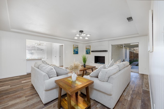 living room with a tray ceiling, a brick fireplace, dark hardwood / wood-style floors, and an inviting chandelier