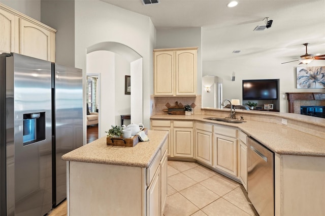 kitchen with kitchen peninsula, stainless steel appliances, sink, a fireplace, and light tile patterned flooring