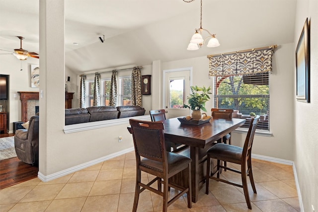 tiled dining room featuring a fireplace, ceiling fan with notable chandelier, and lofted ceiling