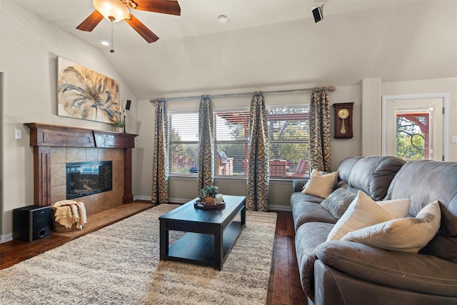 living room with a tile fireplace, ceiling fan, dark wood-type flooring, and vaulted ceiling