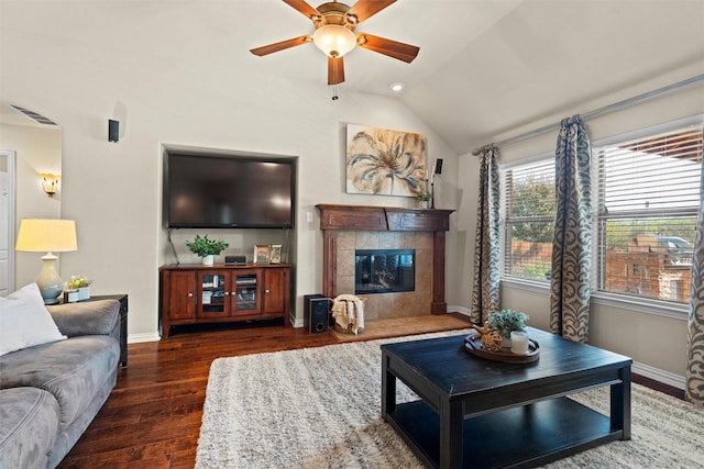 living room with a tile fireplace, vaulted ceiling, ceiling fan, and dark wood-type flooring