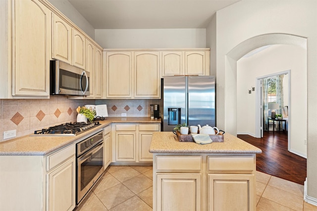 kitchen with decorative backsplash, a kitchen island, light tile patterned floors, and appliances with stainless steel finishes