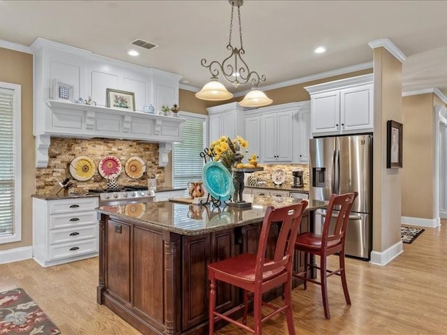 kitchen with crown molding, dark stone counters, stainless steel fridge, a kitchen island, and backsplash