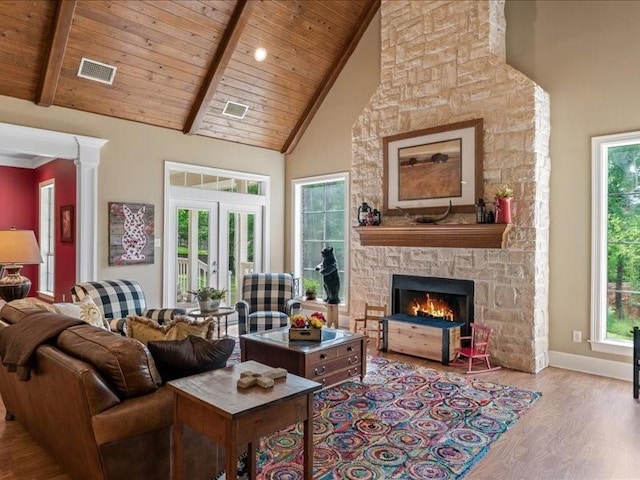 living room with high vaulted ceiling, beam ceiling, light wood-type flooring, wooden ceiling, and a stone fireplace